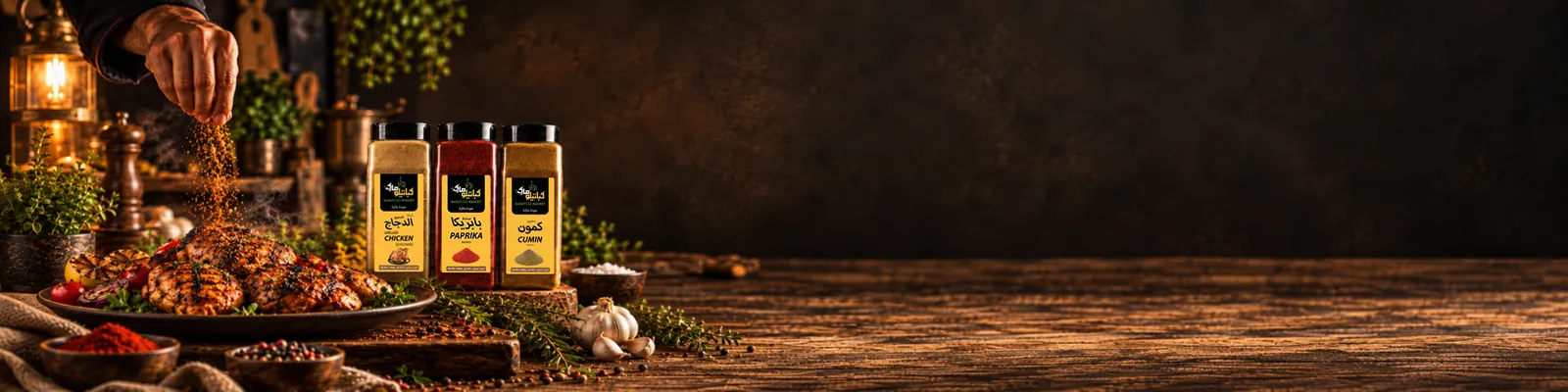 يد ترش التوابل على دجاج مشوي، وبجانبه عبوات كباتيلو ماركت لتتبيلة الدجاج المشوي والبابريكا المدخنة والكمون المطحون