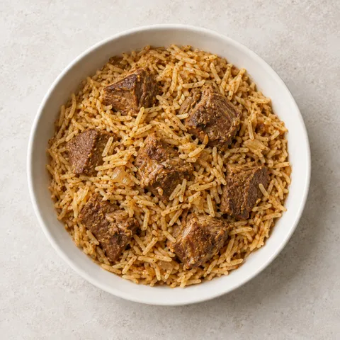 صورة توضيحية لأرز بسمتي متبل مع قطع لحم ضأن بنية بلا عظم وبصل مطهو، في وعاء أبيض مائل للعاجي على سطح فاتح، من الأعلى.